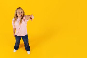 Cute preteen girl pointing forward with excitement on yellow studio background. Cheerful child...