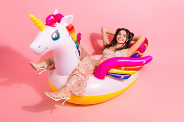 Fun glamorous party scene with a young woman on a rainbow unicorn pool float against pink...