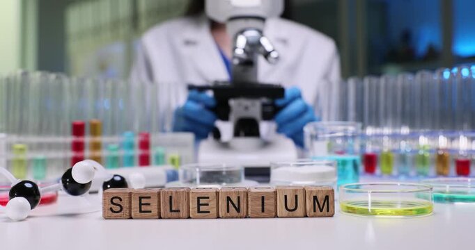 Text Selenium of wooden cubes among glassware with color fluids on chemist workplace. Woman scientist with microscope analyses minerals in laboratory