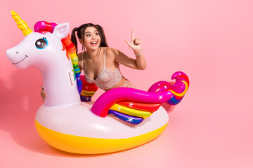 Fototapeta na wymiar Young woman riding a unicorn inflatable float in a pink studio smiles and poses for fashion lifestyle and party promo