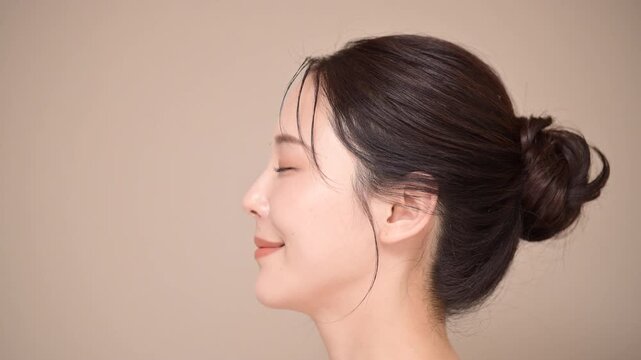 髪の毛がアップ背景がベージュの使いやすい美容やスキンケアの美しい女性のイメージ　目を閉じるクローズアップ横顔スロー
