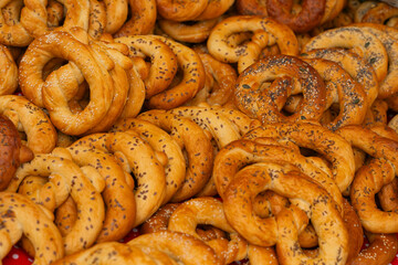 A pile of freshly baked pretzels with various seed and spice toppings, displayed at a market stall.