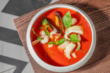 Gourmet seafood soup with shrimp, mussels, white fish and fresh basil served in vibrant tomato broth, top view restaurant presentation