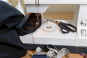 Winter needlework. Hemming the bottom of warm pants at home with a sewing machine. Sewing accessories: scissors, pins, thread, and a measuring tape on the table
