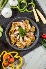 A shrimp dish with chili garlic sauce and vegetable garnish, served on a dark plate with bamboo mat background.