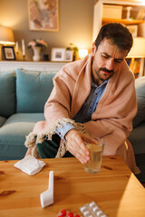 Sick man having flu and fever drinking dissolved effervescent vitamin C tablet in glass of water
