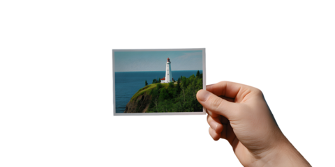Hand holds a photo of split rock lighthouse on a cliff by the deep blue sea isolated on white background