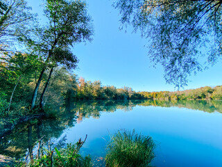 Serene landscape featuring a tranquil lake surrounded by lush greenery and trees, reflecting the clear blue sky, creating a peaceful natural environment for relaxation and contemplation