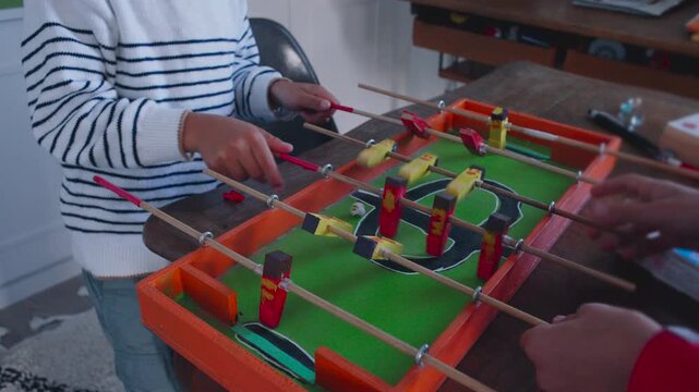 Children playing tabletop foosball game with focused active movement creating lively interactive moment filled with coordination concentration and playful energy in warm home environment