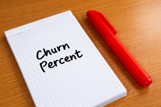 Checkered Notepad with Churn Percent written on it next to a Vibrant Red Marker on a Wooden Desk
