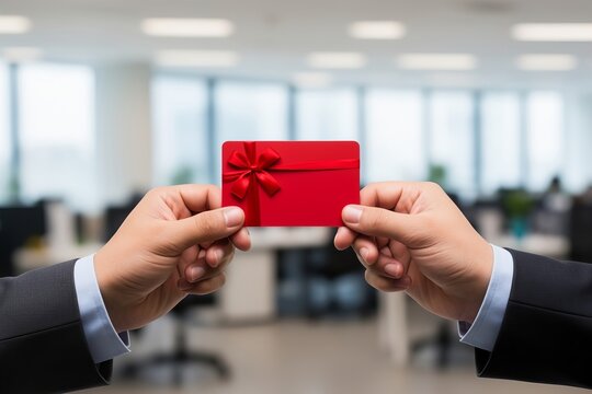 Hands of Two Business Professionals Holding a Red Gift Card in Blurry Office Background