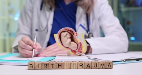 Text Birth Trauma on blocks and human fetus anatomic model in gynecologist office. Physical and psychological distress experienced by mother and baby