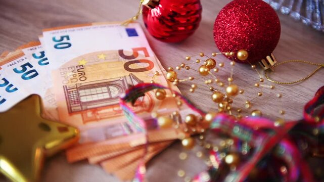 A European cost of Christmas concept with a close up of a stack of 50 Euro bank notes and Christmas decorations on a desk.