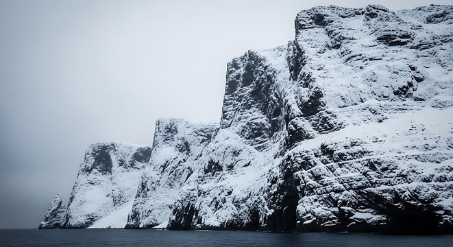 Snow covered cliffs rising from the dark ocean under a gray sky on a cold winter day landscape ai generated
