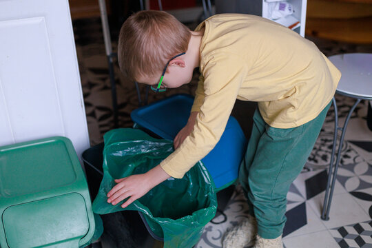 A child adjusts household recycling bins while preparing for waste sorting. Concept of eco education, family sustainability habits and developing responsibility. - Powered by Adobe