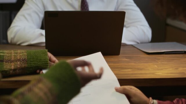Handheld shot of mother and daughter discussing failed math test while sitting in front of male principal during meeting in school office