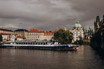 Naklejka premium River cruise boat sailing by historical architecture along a scenic European cityscape.