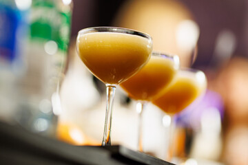 Three Foamy Cocktails in Coupe Glasses at a Bar