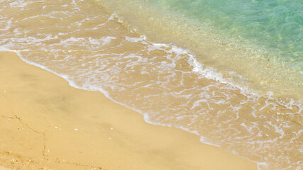Aerial closeup of the waves crashing onto the shoreline of the sandy beach. The coast is empty and there's no one on the beach.