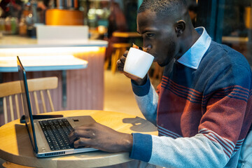 Focused young man enjoys coffee while working on laptop at a cozy cafe