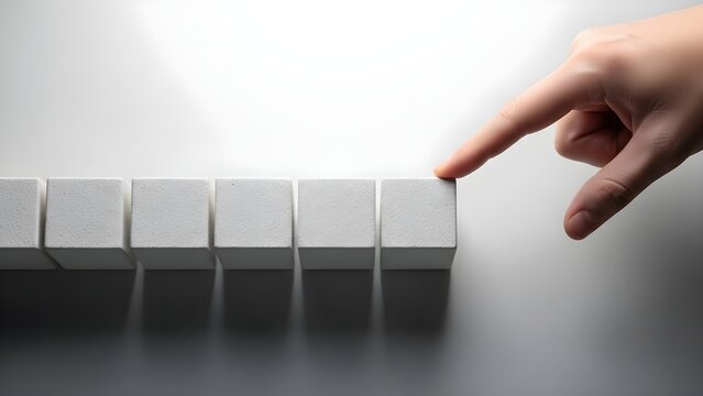 A human hand gently touches the last of a row of six white blocks, suggesting the completion of a sequence or the start of a domino effect. This visual concept provides Daily encouragement for tackli