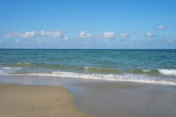 Vast Lang Co Beach with golden sand, gentle blue waves, and tall palm trees under a bright, sunny, cloud dotted sky.
