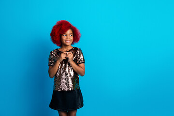 Young girl with red hair wearing a shiny sequin top standing against a bright blue background smiling and posing for a fashion lifestyle image