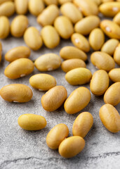Heirloom dry yellow Mayocoba beans (Phaseolus vulgaris) scattered on a light surface with smooth texture and natural color. Minimal food concept of legumes, plant-based protein and healthy cooking. 