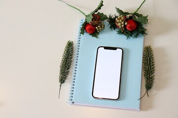 Smartphone with blank screen on notebook with christmas decoration. Social media mock up. 