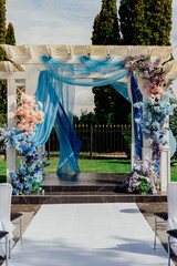 Elegant outdoor wedding arch with blue drapery and floral decorations on a sunny day