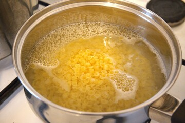 Small shell pasta cooking in water inside a cooking pan in close-up, showing homemade soup preparation.