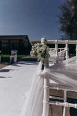 Elegant wedding ceremony setup with white chairs and floral decorations in outdoor setting.