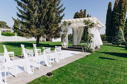 Elegant outdoor wedding ceremony setup with floral decorated arch and white chairs