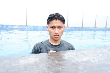 Young man with dark wet hair wearing a dark tshirt submerged in a swimming pool with clear blue water, looking directly at the camera with a serious expression