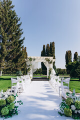 Elegant outdoor wedding ceremony with decorated aisle and flower arch in a garden setting.