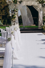 Elegant outdoor wedding ceremony setup with white floral decorations and draped chairs.