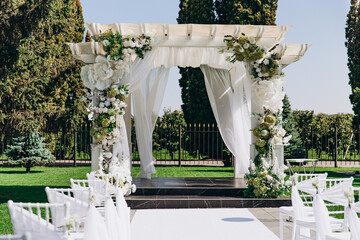 Elegant outdoor wedding ceremony setup with floral arch and white chairs.
