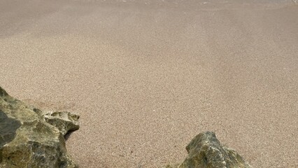 A close-up view of textured golden sand on a beach with rugged rocks in the foreground.