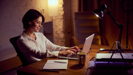 Woman typing on laptop during relaxed evening work session. Concept of hybrid office, digital communication flow, creative remote tasks, and confident female leadership mindset.