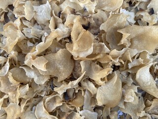Close-up view of a large pile of dried, light brown, wavy, and thin food pieces, possibly dried mushrooms or snacks, showing their delicate texture.