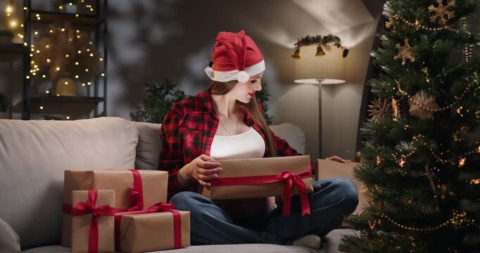 A pregnant woman opens a Christmas gift revealing ultrasound images, celebrating the upcoming arrival of her baby. A woman in a Santa hat opens a gift box - Powered by Adobe