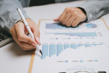 Business chart analysis person holding pen financial report data visualization office desk laptop keyboard business strategy blue bar graph pie chart business document professional workspace