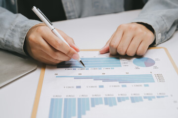 Person analyzing chart with pen, business report on clipboard, data visualization with bar graph and pie chart, office desk setting, financial review and planning