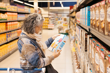 Senior woman reading label of cereal box in supermarket