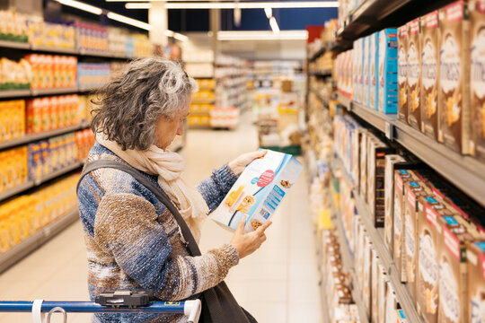 Senior woman reading label of cereal box in supermarket