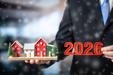 Businessman holds a houses with Christmas tree and numbers 2026. Concept for greetings with a Happy...