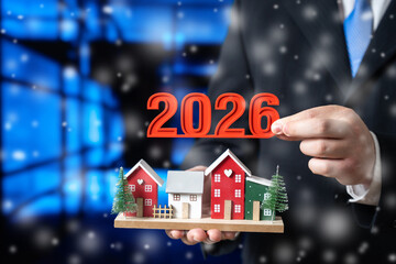 Businessman holds a houses with Christmas tree and numbers 2026. Concept for greetings with a Happy...