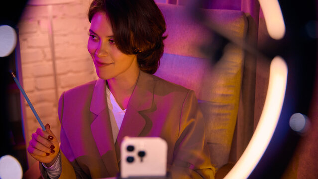 Woman smiling at phone through ring light during coaching video. Concept of friendly digital presence, brand warmth, and trust-building online communication.