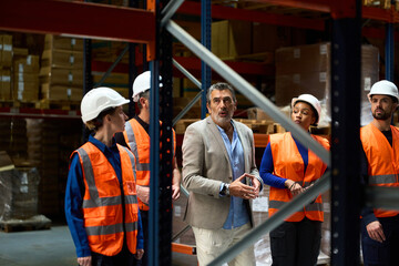 Manager talking with diverse warehouse workers in safety gear