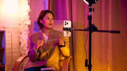 Woman talking while holding pencil in digital coaching setup. Concept of thoughtful mentoring, expressive communication, and interactive online teaching.